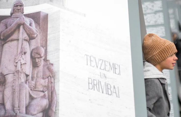 Zēns pie uzraksta Tēvzemei un Brīvībai un fragmenta no Brīvības pieminekļa.