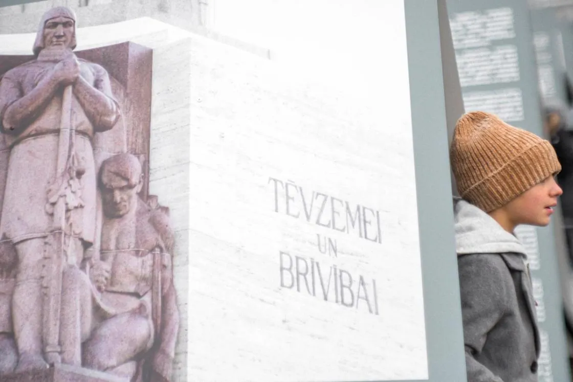 Zēns pie uzraksta Tēvzemei un Brīvībai un fragmenta no Brīvības pieminekļa.